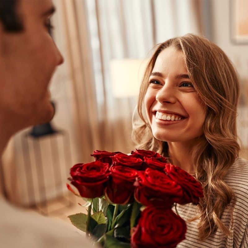 A smiling woman being given a bouquet of red roses