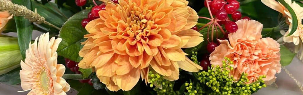 Autumn flower bouquet of orange and red flowers with green foliage and red berries