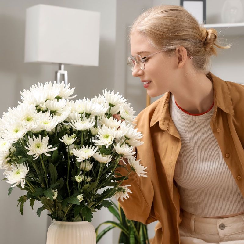 Woman leaning over a vase of white chrysanthemums and smiling