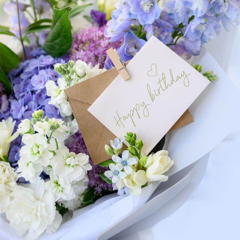 A bouquet of purple and white flowers with a Happy Birthday card in them