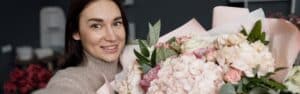A woman taking a selfie holding a large bouquet of soft pink and white flowers